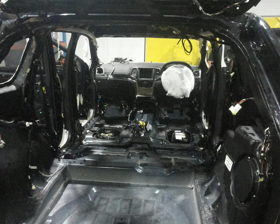 A vehicle interior stripped down to the bare shell, with wiring loose and the steering wheel airbag deployed