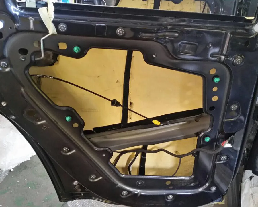 The inside of a vehicle door with its trim removed, exposing the frame, wiring and window regulator