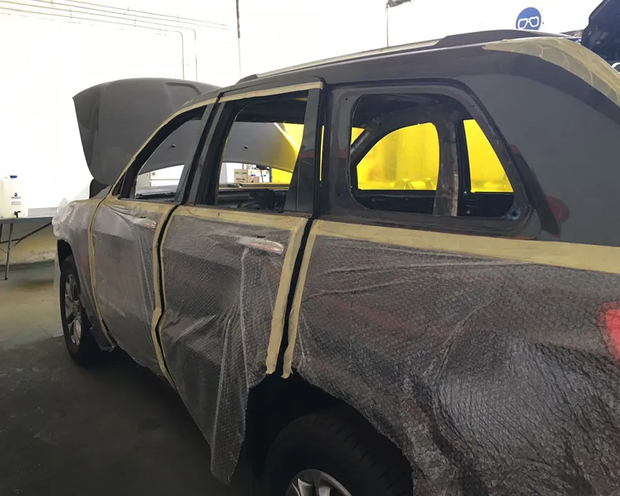 An SUV in the workshop with its doors masked in plastic and tape, yellow screens visible through the windows