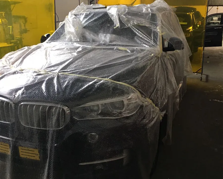 A dark BMW SUV wrapped in clear protective plastic in the workshop