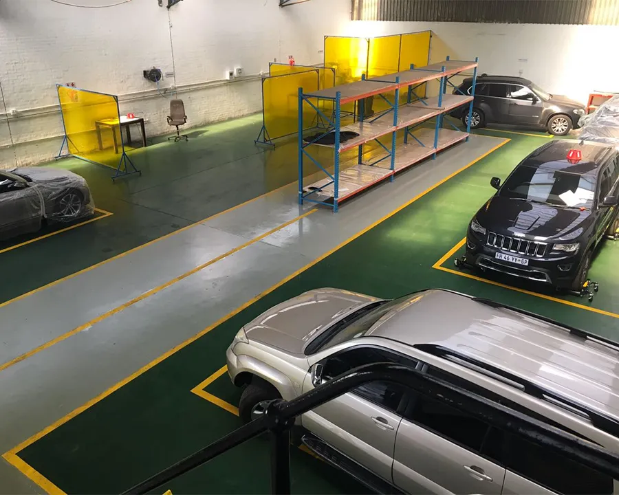The Armour Pro workshop floor seen from above: green epoxy floor with yellow bay lines, yellow welding screens, shelving, and SUVs in the bays