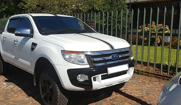 A white double-cab bakkie with tinted windows parked on a brick driveway
