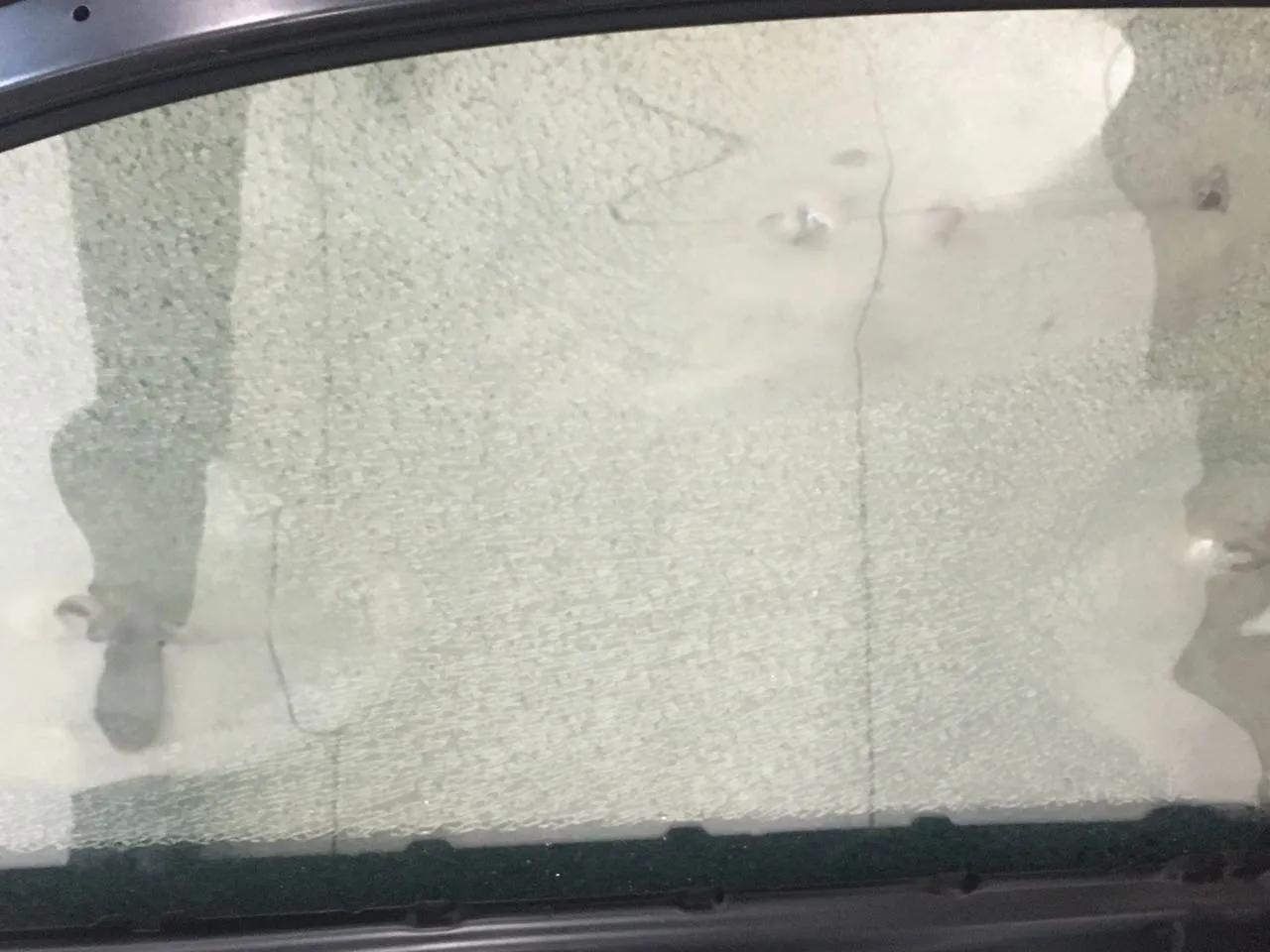 A side window with ResistaMate installed, crazed across its surface after being shot with a 9mm handgun, still in one piece in its frame
